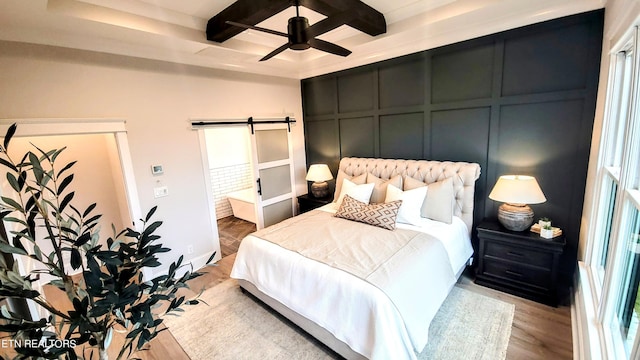 bedroom featuring a barn door, coffered ceiling, wood finished floors, a decorative wall, and beam ceiling