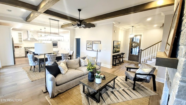 living room featuring baseboards, ceiling fan, beamed ceiling, stairs, and light wood-type flooring