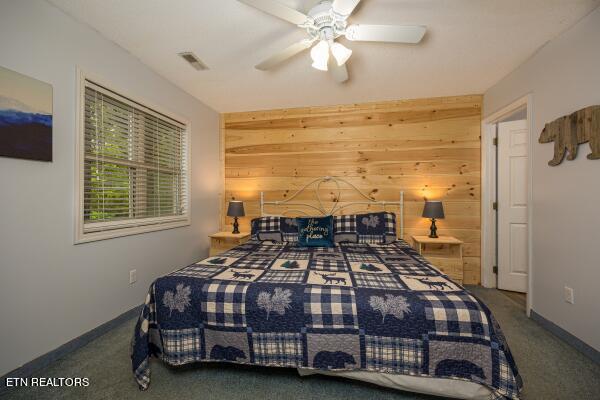 bedroom with ceiling fan, dark carpet, and wooden walls