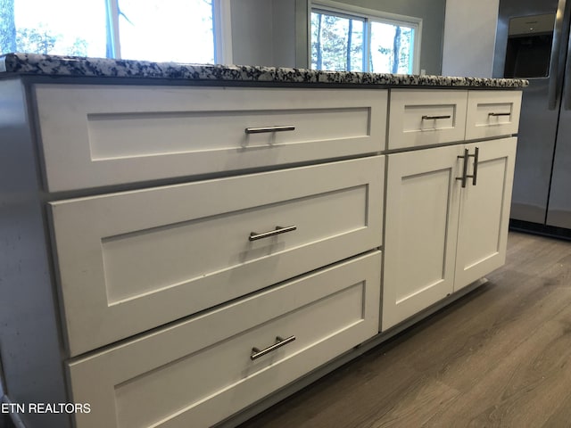 room details featuring white cabinets, dark hardwood / wood-style floors, dark stone countertops, and stainless steel refrigerator