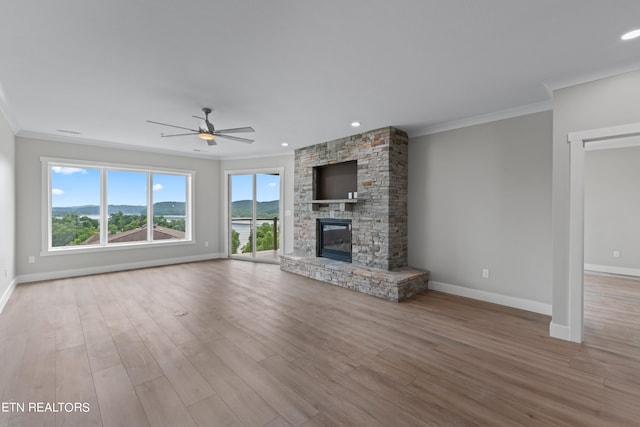 unfurnished living room featuring crown molding, a stone fireplace, ceiling fan, and hardwood / wood-style floors