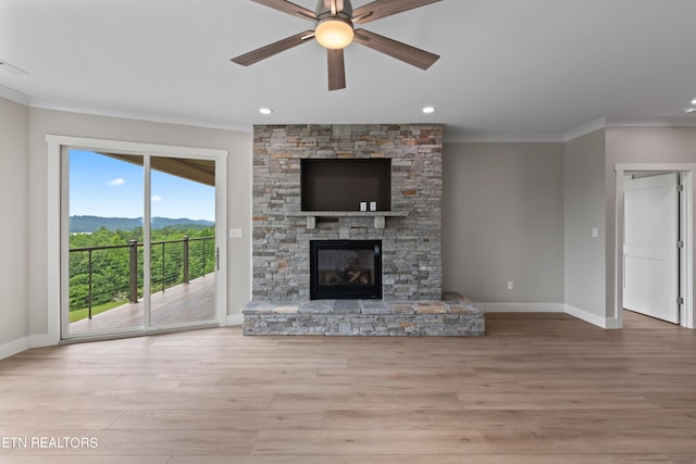 unfurnished living room with a stone fireplace, ornamental molding, ceiling fan, and light hardwood / wood-style flooring