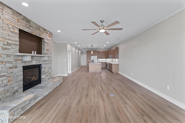 unfurnished living room featuring a fireplace, ceiling fan, light wood-type flooring, and crown molding