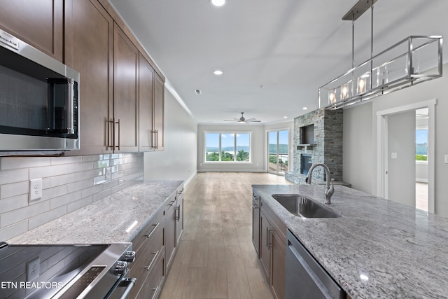 kitchen featuring ceiling fan, light hardwood / wood-style floors, stainless steel appliances, a fireplace, and sink