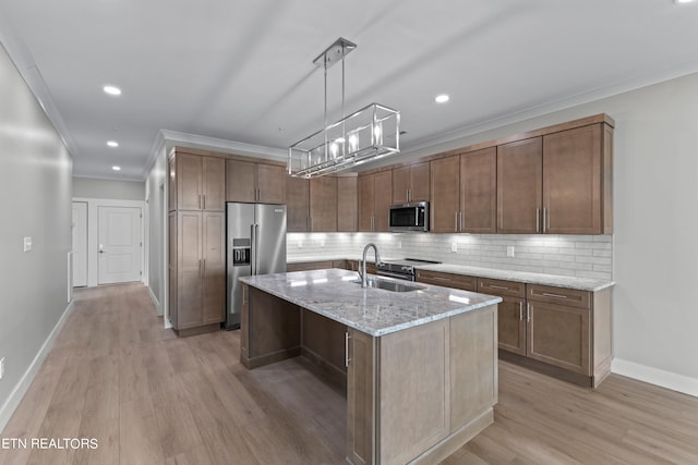 kitchen featuring light stone countertops, light hardwood / wood-style flooring, backsplash, premium appliances, and a kitchen island with sink