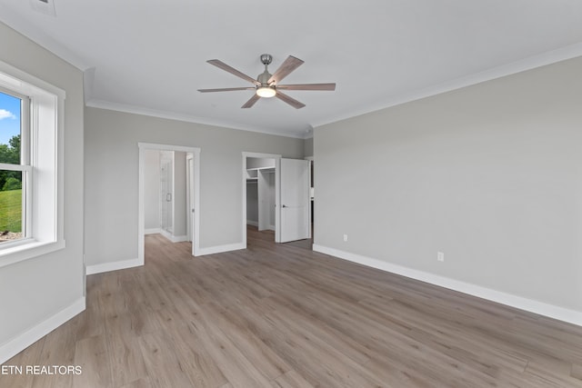 unfurnished bedroom featuring a closet, ceiling fan, crown molding, hardwood / wood-style floors, and a walk in closet