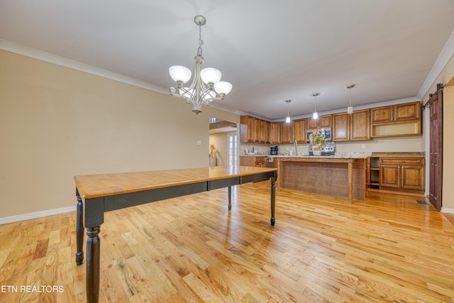 kitchen featuring an inviting chandelier, a barn door, light wood-type flooring, pendant lighting, and ornamental molding