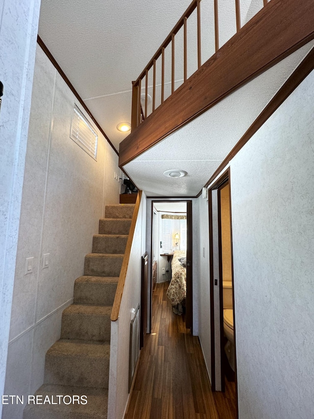 stairs featuring a textured ceiling, ornamental molding, and dark hardwood / wood-style floors