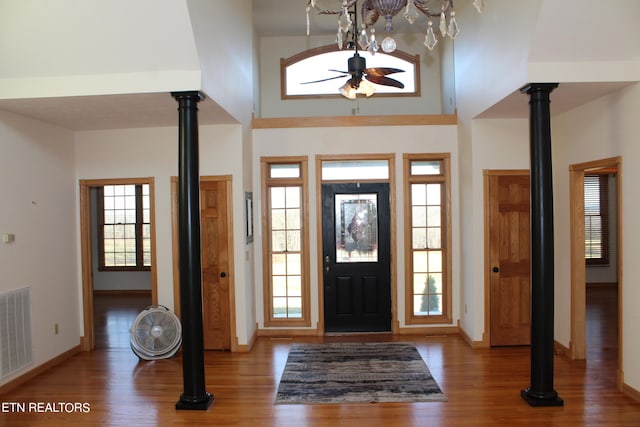 entrance foyer featuring hardwood / wood-style floors, decorative columns, a towering ceiling, and ceiling fan with notable chandelier