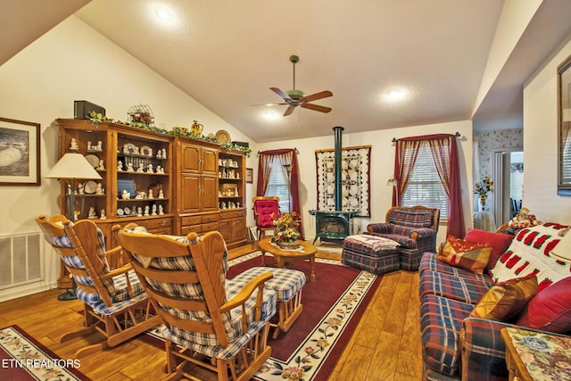 living room featuring hardwood / wood-style flooring, ceiling fan, lofted ceiling, and a wood stove