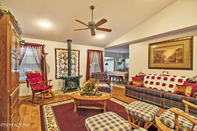 living room with hardwood / wood-style flooring, ceiling fan, a textured ceiling, vaulted ceiling, and a wood stove