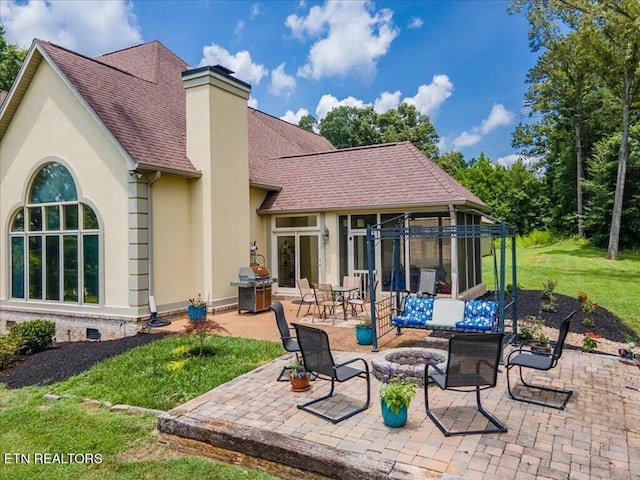 back of property with a fire pit, a yard, and a patio