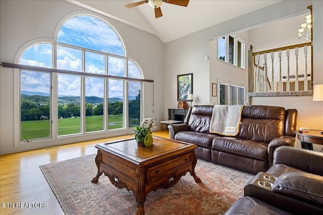 living room with high vaulted ceiling, ceiling fan with notable chandelier, and light hardwood / wood-style flooring