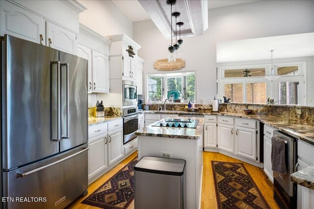 kitchen featuring a kitchen island, stainless steel appliances, dark stone countertops, decorative light fixtures, and white cabinetry