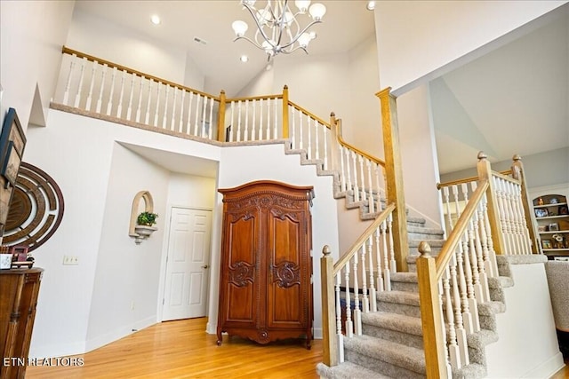 stairway with an inviting chandelier, high vaulted ceiling, and light hardwood / wood-style floors