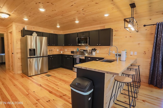 kitchen with a breakfast bar, wood ceiling, a sink, a peninsula, and appliances with stainless steel finishes