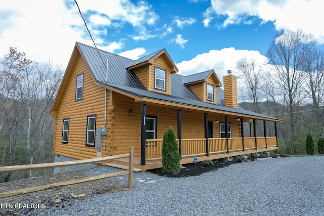 view of front of house with metal roof, a chimney, a porch, and log exterior