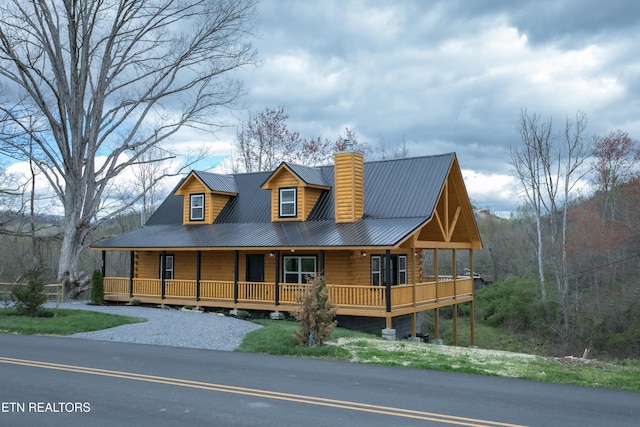 view of front of property with log siding, metal roof, a chimney, and a porch