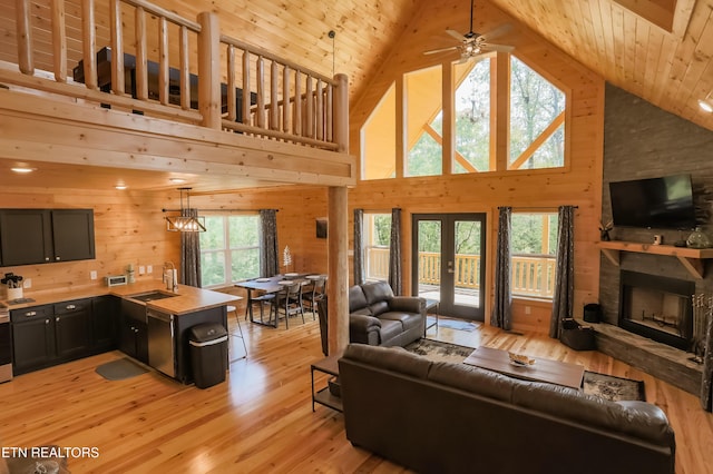 living room with french doors, a fireplace, wooden walls, light wood-style flooring, and ceiling fan