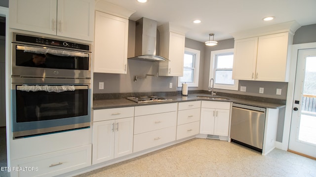 kitchen with appliances with stainless steel finishes, white cabinetry, wall chimney exhaust hood, and sink