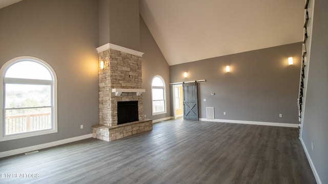 unfurnished living room featuring high vaulted ceiling, dark hardwood / wood-style flooring, a stone fireplace, and a barn door