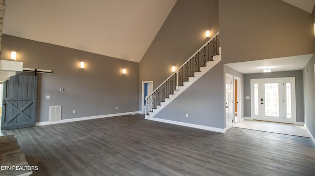 unfurnished living room featuring dark hardwood / wood-style flooring, high vaulted ceiling, and a barn door