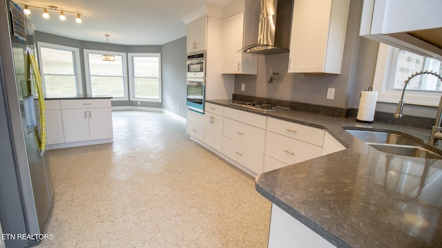 kitchen featuring pendant lighting, stainless steel appliances, wall chimney range hood, white cabinetry, and sink