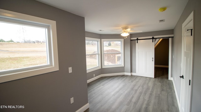 unfurnished room featuring a barn door, hardwood / wood-style floors, and ceiling fan