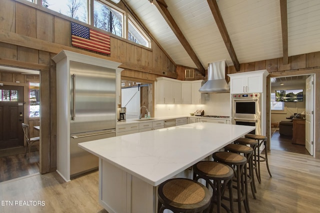 kitchen featuring white cabinetry, stainless steel appliances, a center island, and wall chimney exhaust hood