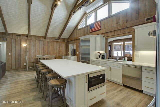 kitchen with appliances with stainless steel finishes, sink, light wood-type flooring, white cabinets, and a kitchen island