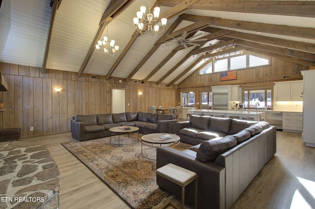 living room featuring light hardwood / wood-style floors, high vaulted ceiling, beamed ceiling, ceiling fan with notable chandelier, and wooden walls