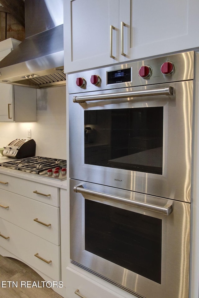kitchen with stainless steel appliances, white cabinetry, and wall chimney range hood