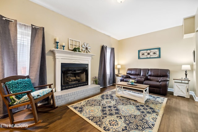 living area featuring baseboards, a brick fireplace, and wood finished floors