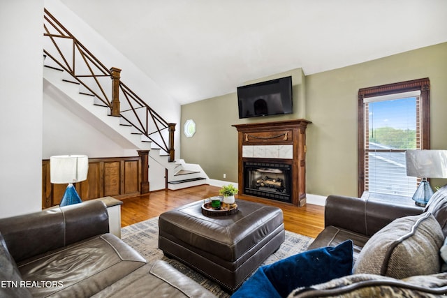 living area with stairway, vaulted ceiling, wood finished floors, a tiled fireplace, and baseboards