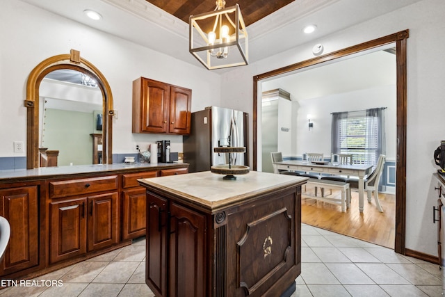 kitchen featuring a center island, light tile patterned floors, stainless steel fridge with ice dispenser, a tray ceiling, and a notable chandelier