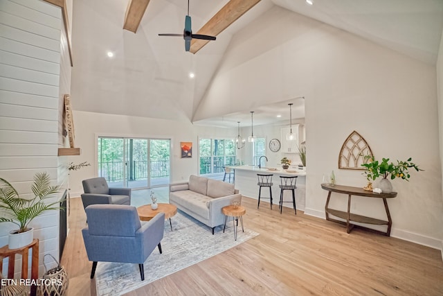 living room featuring beam ceiling, sink, light hardwood / wood-style flooring, high vaulted ceiling, and ceiling fan with notable chandelier