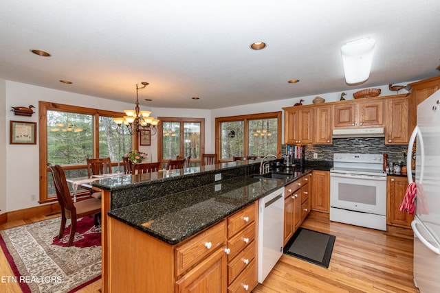 kitchen featuring white appliances, dark stone counters, sink, decorative light fixtures, and a chandelier