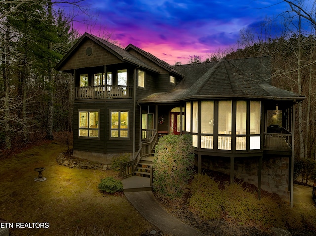 back house at dusk with a balcony and a sunroom