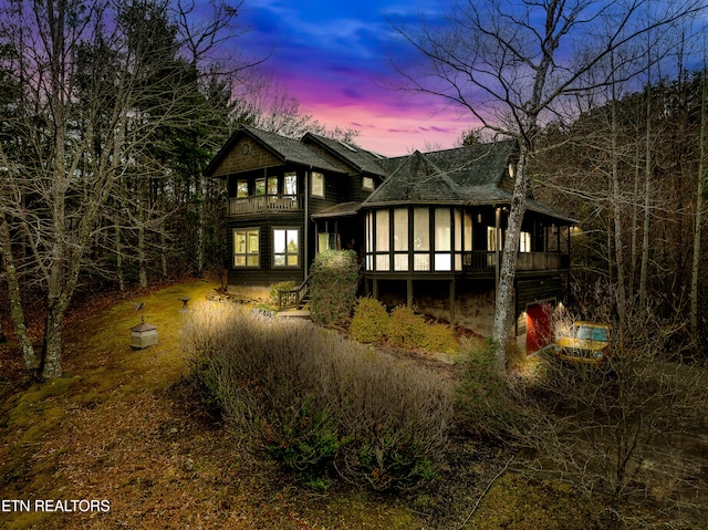 back house at dusk featuring a sunroom and a balcony