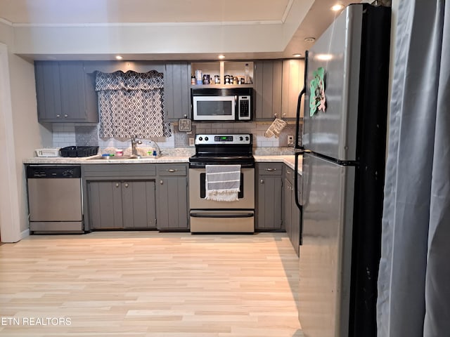 kitchen with backsplash, sink, light wood-type flooring, stainless steel appliances, and gray cabinets