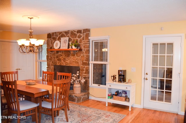 dining space with a stone fireplace, light wood-type flooring, and an inviting chandelier