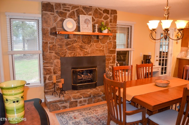 dining space featuring a healthy amount of sunlight, hardwood / wood-style floors, a stone fireplace, and a chandelier