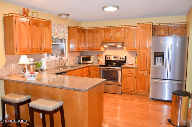 kitchen featuring light wood-type flooring, appliances with stainless steel finishes, wall chimney exhaust hood, sink, and tasteful backsplash