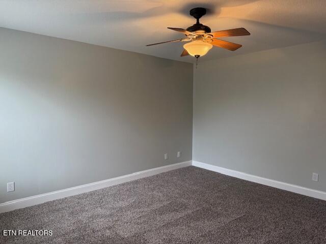 unfurnished room with baseboards, dark carpet, and a ceiling fan