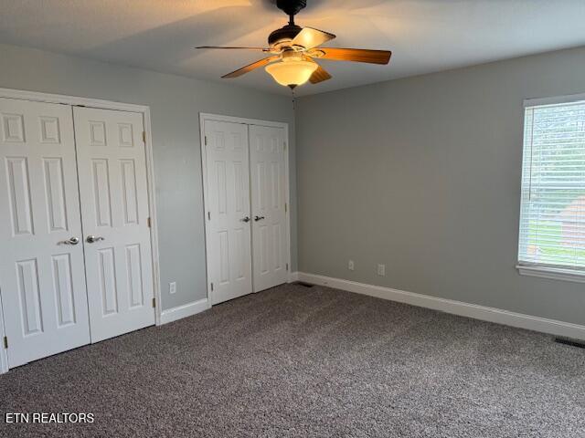 unfurnished bedroom with baseboards, visible vents, two closets, ceiling fan, and carpet