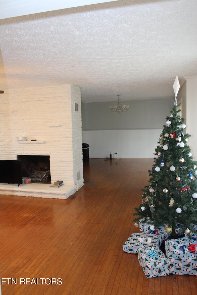 unfurnished living room with a notable chandelier, a textured ceiling, dark wood-type flooring, and a fireplace