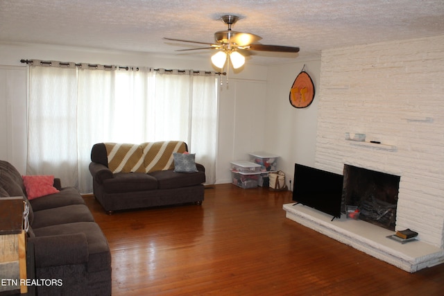 living room with dark hardwood / wood-style flooring, ceiling fan, a fireplace, and a textured ceiling