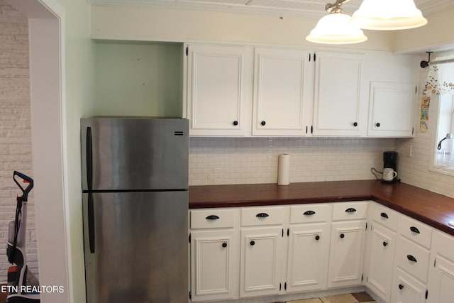 kitchen with backsplash, ornamental molding, stainless steel refrigerator, and white cabinetry