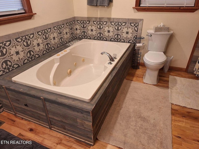 bathroom with toilet, hardwood / wood-style floors, and a bath to relax in