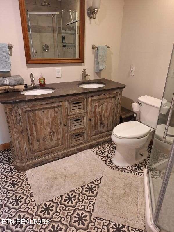 bathroom featuring double vanity, toilet, tile floors, and a shower with shower door